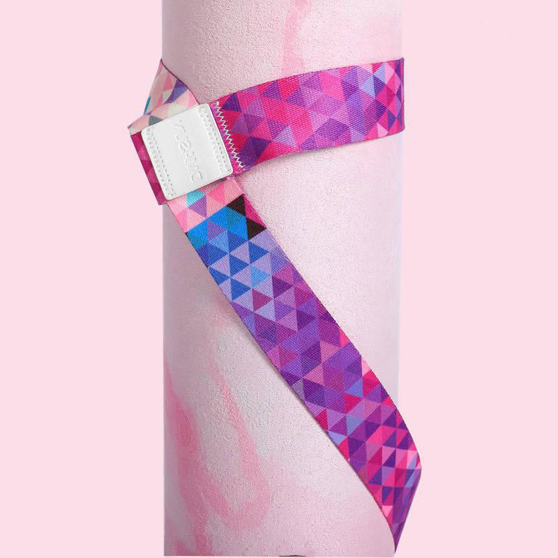 Close-up of a cotton yoga mat strap wrapped around a rolled yoga mat. Features a secure fit with a vibrant pink and purple geometric design.